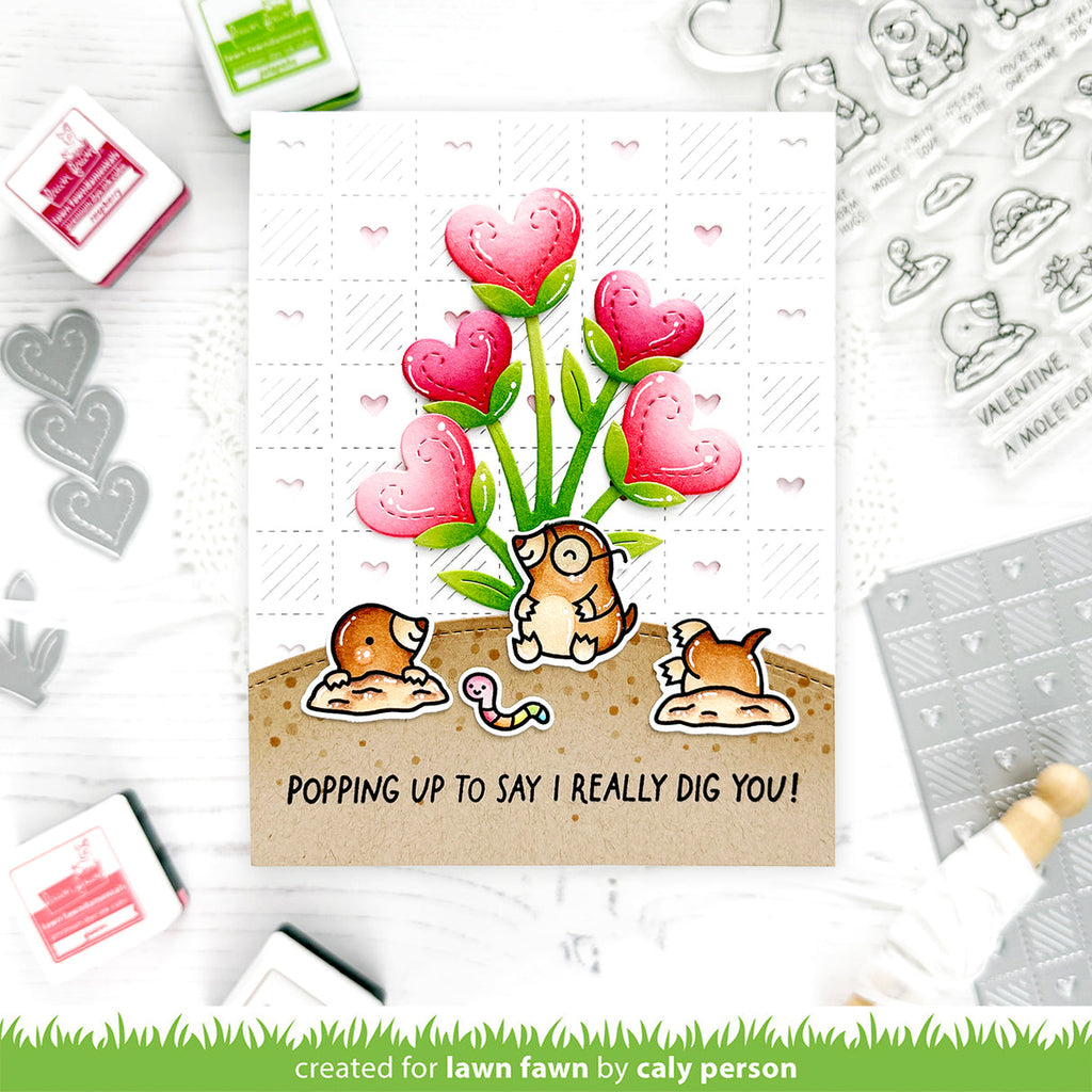 Valentine's Day card with cartoon moles and heart-shaped flowers, surrounded by stamping tools.