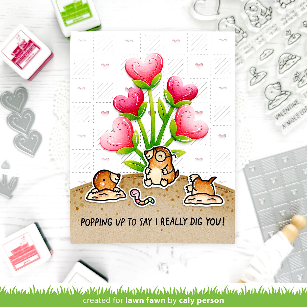 Valentine's Day card with cartoon moles and heart-shaped flowers, surrounded by stamping tools.
