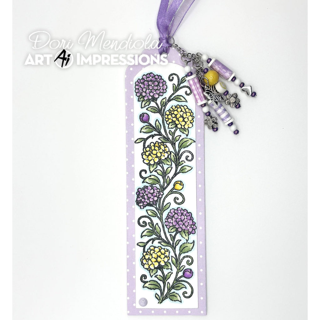 A decorative paper bookmark featuring a hand-drawn purple and yellow floral vine pattern on a white background with a light purple border. The bookmark is adorned with a purple ribbon loop, silver-toned metal charms, and colorful beads
