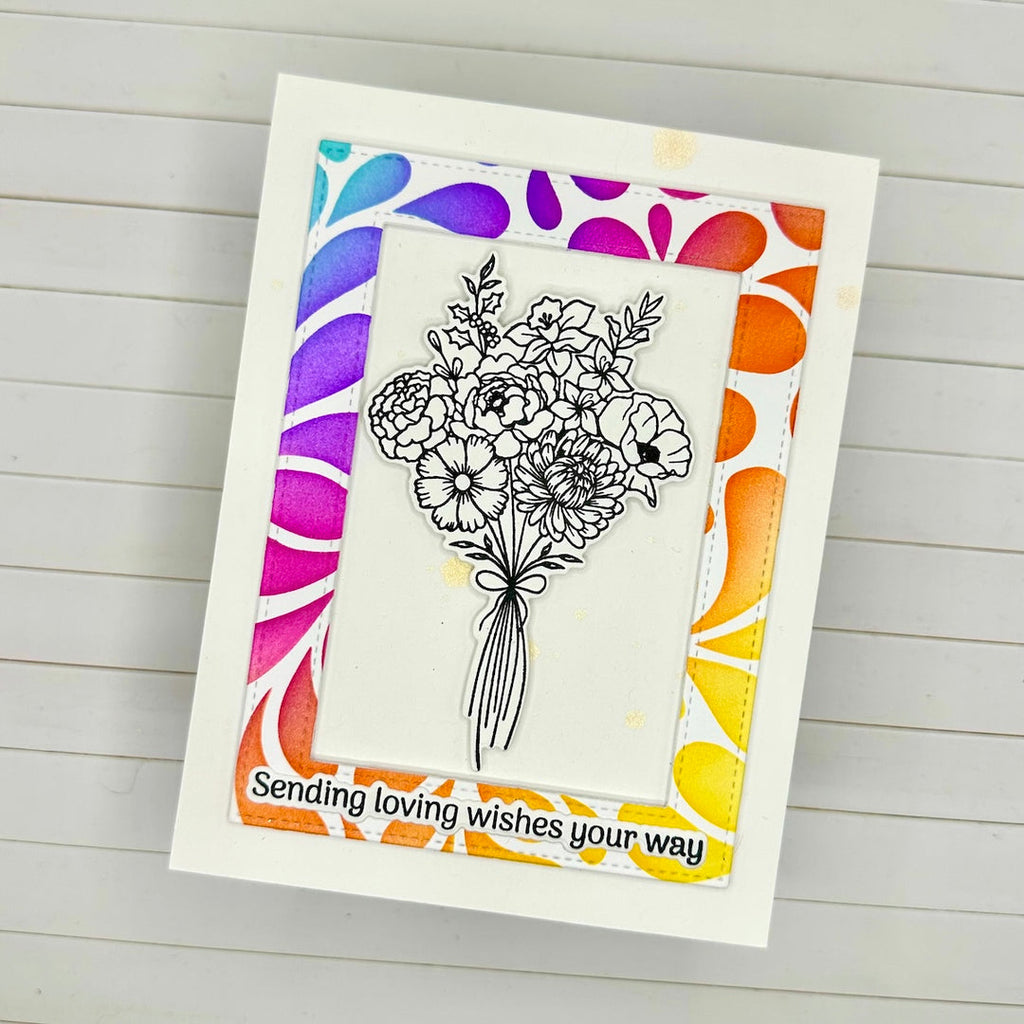 A handmade greeting card featuring a black-and-white floral bouquet illustration in the center, surrounded by a colorful rainbow gradient border on a white cardstock background. The bottom reads, 'Sending loving wishes your way'.