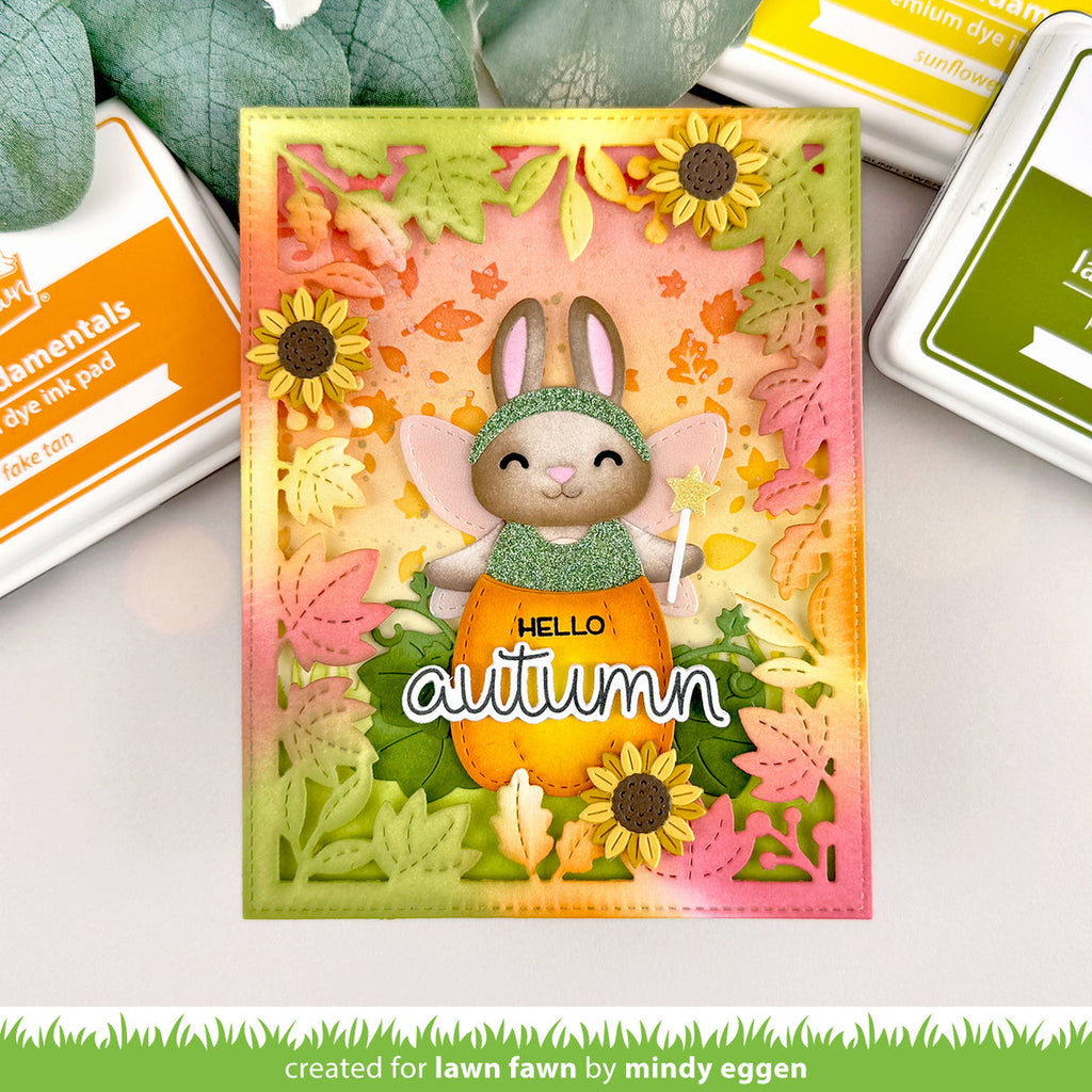 Autumn-themed card with a rabbit in an orange outfit and sunflowers, surrounded by stamping supplies. | color-code:alt1