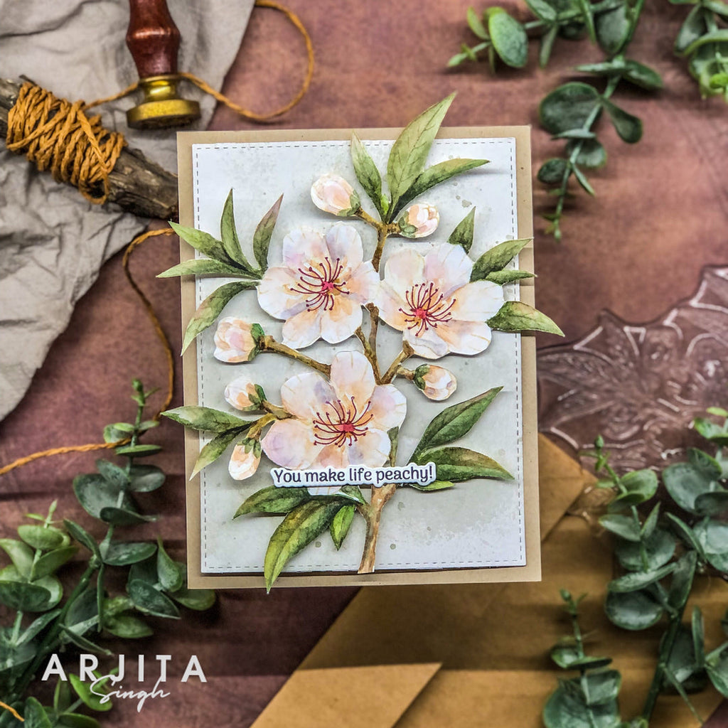 Card with floral design and text 'You make life peachy!' on a textured surface with greenery.