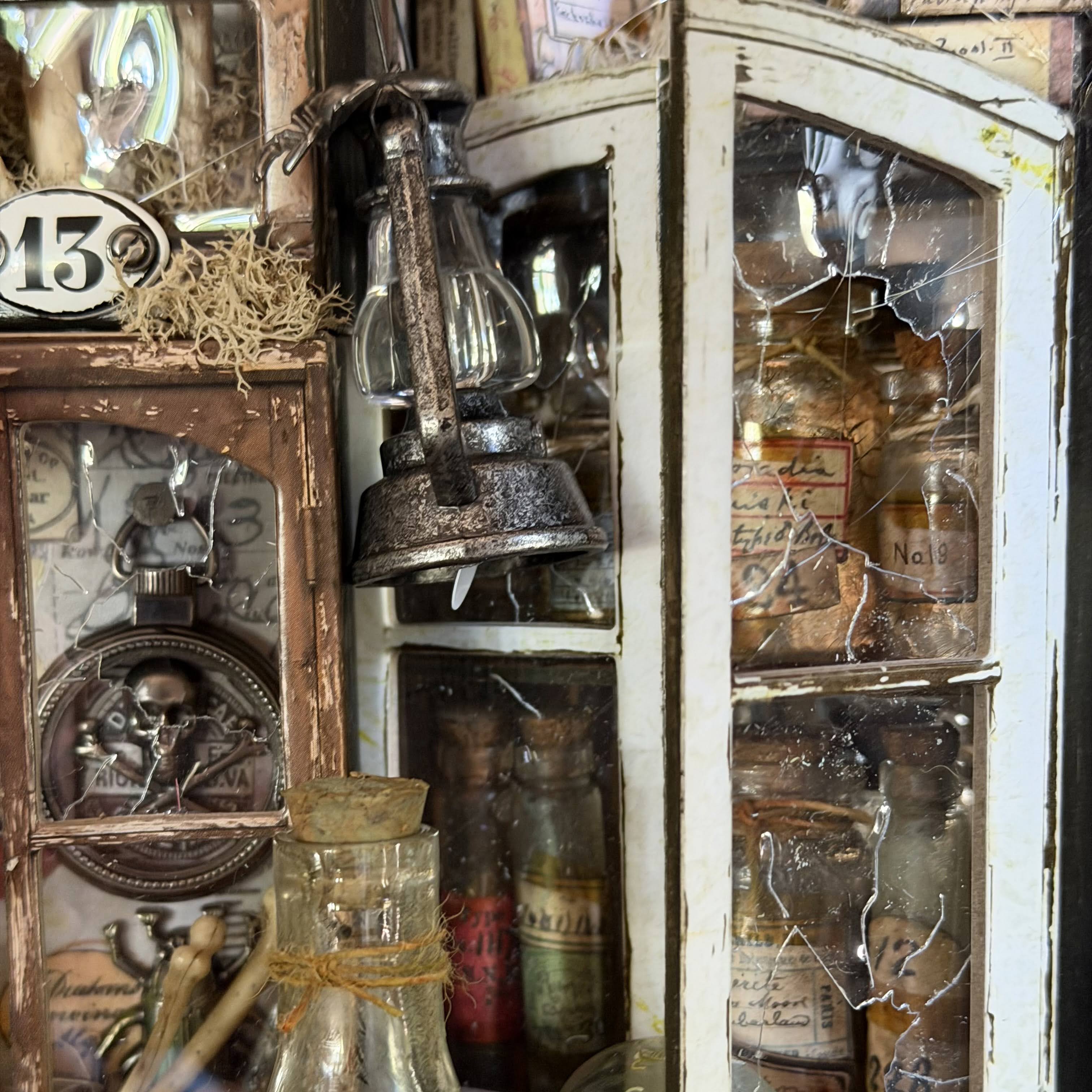 A rustic vintage-style decorative cabinet or wall display filled with antique glass bottles, jars, a hanging lantern, and distressed wood panels. The scene is tightly framed and appears to show the product as a styled decor arrangement rather than a clean isolated studio shot.