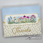 A handmade greeting card with a blue and white gingham patterned top section, a central floral illustration panel with pink, purple, yellow, and white flowers, and a lower cream section with green leaf print and gold foil script reading 'Thanks.'