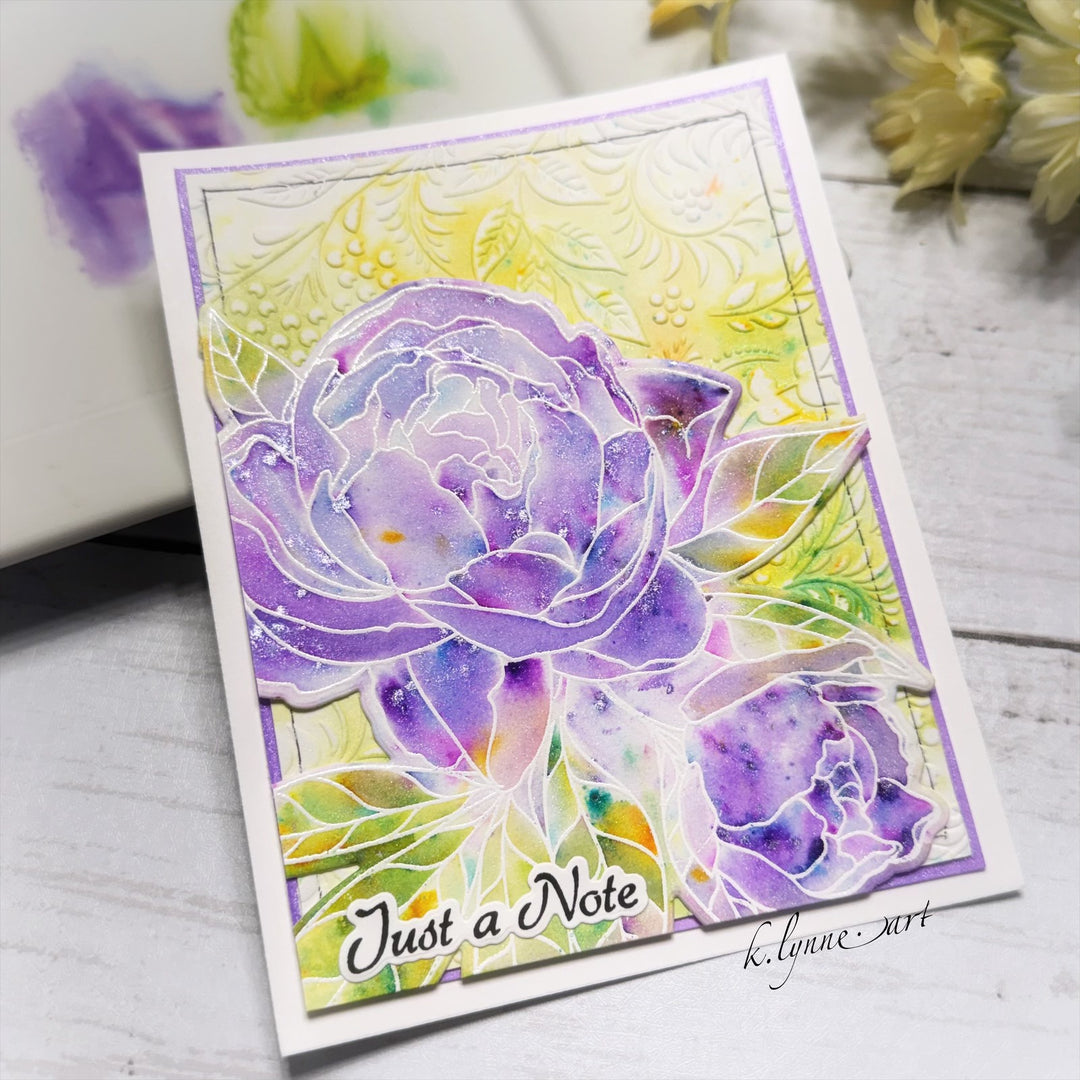 Greeting card with purple floral design and 'Just a Note' text on a wooden surface.