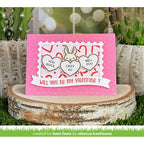 Valentine's Day card with bunnies and hearts on a pink background, placed on a wooden stump with a blurred natural background.