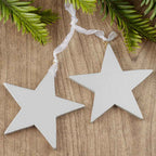 Two silver star-shaped ornaments on a wooden surface with greenery.